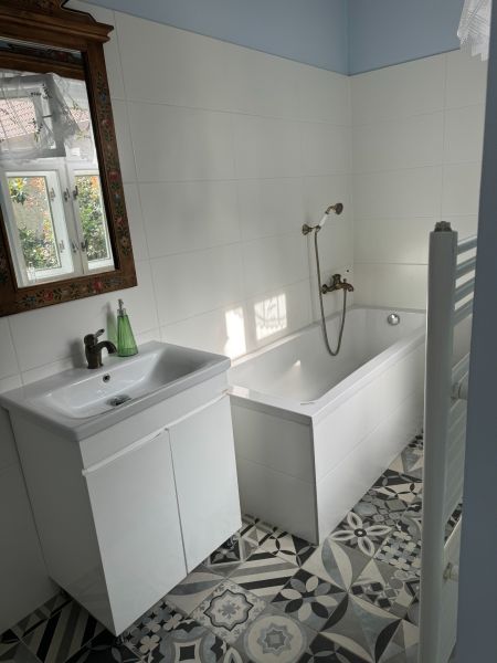 A bathroom in a family house with a white bathtub, sink, and decorated mirror.