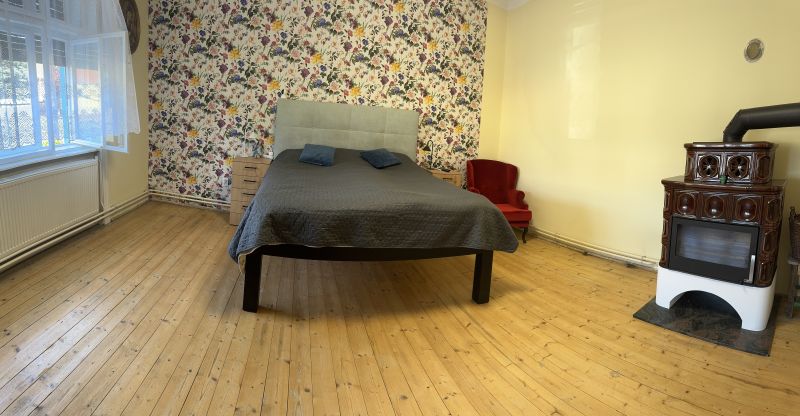 Bedroom with a bed, floral wallpaper, wood-patterned flooring, and a tiled stove.