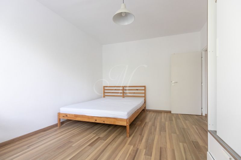 A bedroom with a bed and a wooden decor floor in a three-room apartment.