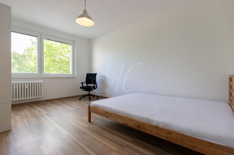 Bright bedroom in a 3-room apartment with wood-patterned flooring and large windows.