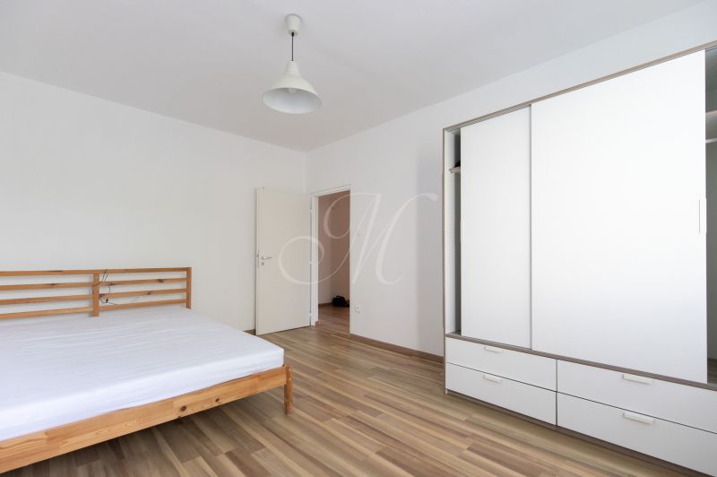 A bedroom with a wooden bed, a white wardrobe, and a floor with a wooden decor in a 3-room apartment.