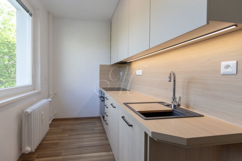 The kitchen in a 3-room apartment with a wooden decor floor and light cabinets.