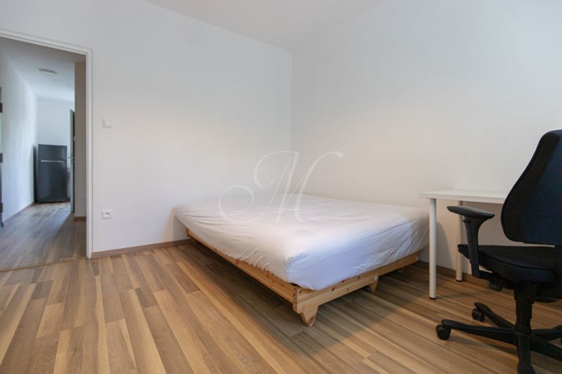A bedroom in a 3-room apartment with a bed, a desk, and a floor with a wooden decor.