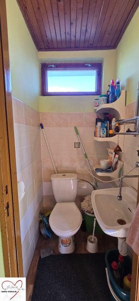 Small bathroom in a cottage with a toilet, sink, and lots of cleaning supplies.