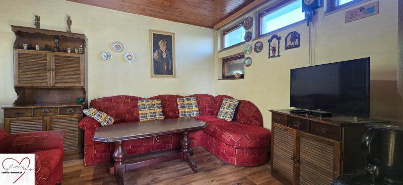 Living room of the cottage with a red sofa, wooden furniture, and a floor with a wooden design.