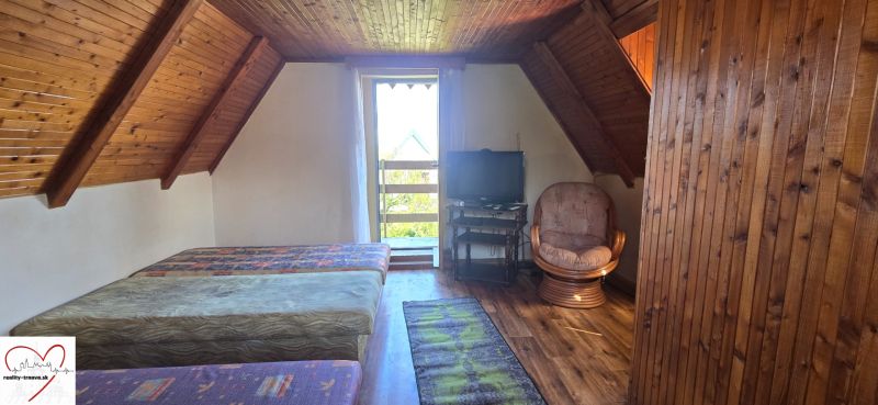 The attic of the cottage with beds, a television, and a floor with a wooden decor.