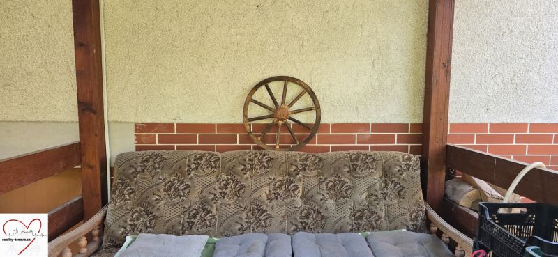 A comfortable sofa on the cottage veranda with wooden elements, a wheel on the wall.