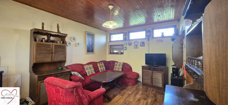 Living room of the cottage with a red sofa, wooden furniture, and a floor with a wooden decor.