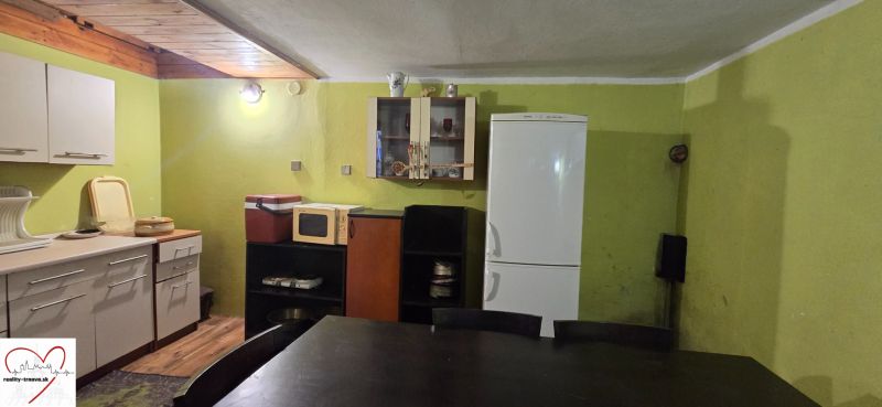 A kitchen in a cottage with green walls, a refrigerator, and a kitchen unit.
