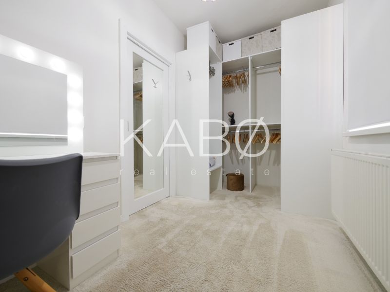 A wardrobe in a family house with white cabinets and a lighted mirror.