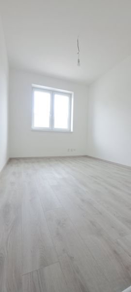 A room with white walls, a wooden decor floor, and a window in a family house.