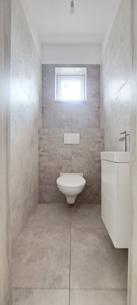 A toilet in a family house with tiles and a small window.