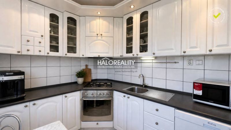 White kitchen with a dark countertop in a 3-room apartment, complemented by built-in appliances.