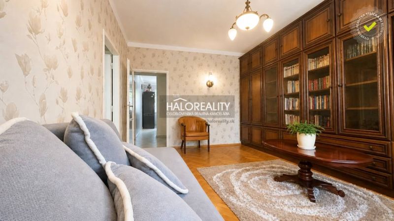 Living room with a bookshelf, sofa, and wooden decor flooring in a three-room apartment.