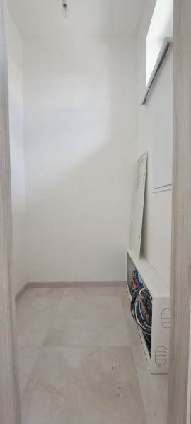 Narrow room with a distribution board in a family house, light tiles, neutral walls.