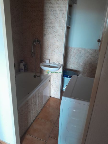 A bathroom in a studio apartment with a bathtub, sink, washing machine, and mosaic tiles.