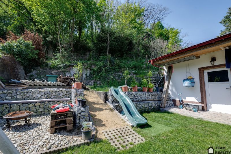 A family house in Potzneusiedl with a courtyard, slide, and stone walls surrounded by greenery.