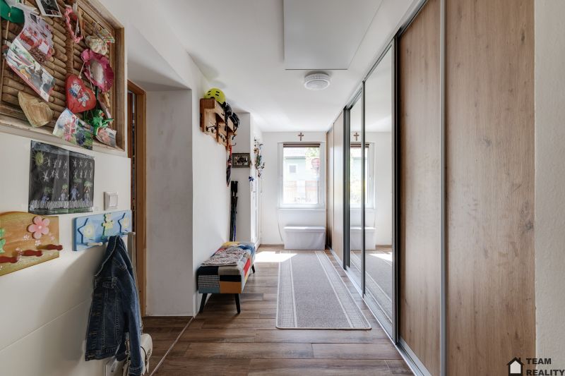Hallway of a family house with coat hooks and a mirror, floor with wooden decor.