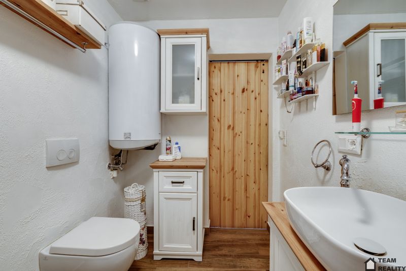 A bathroom in a family house with a toilet, sink, and cabinets, with a wooden decor floor.