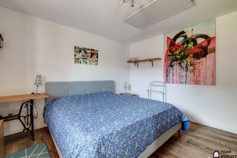 Bedroom in a family house with a bed, wooden decor flooring, and an art painting.