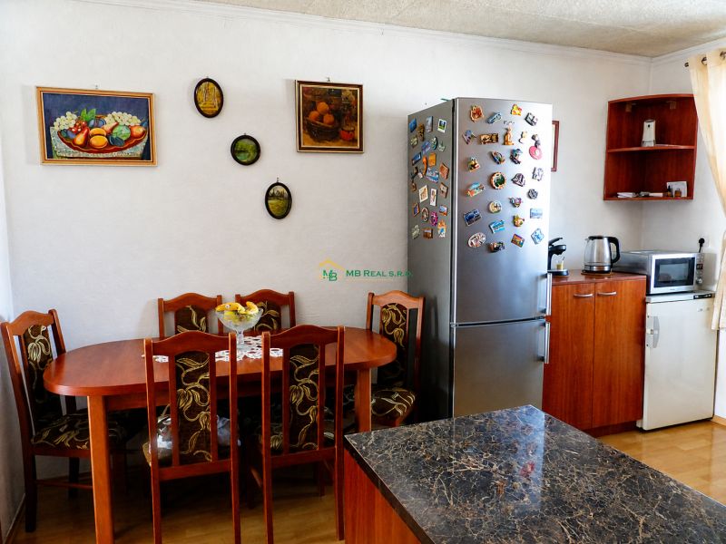A kitchen in a 2-room apartment with a table, refrigerator, and wall decorations.
