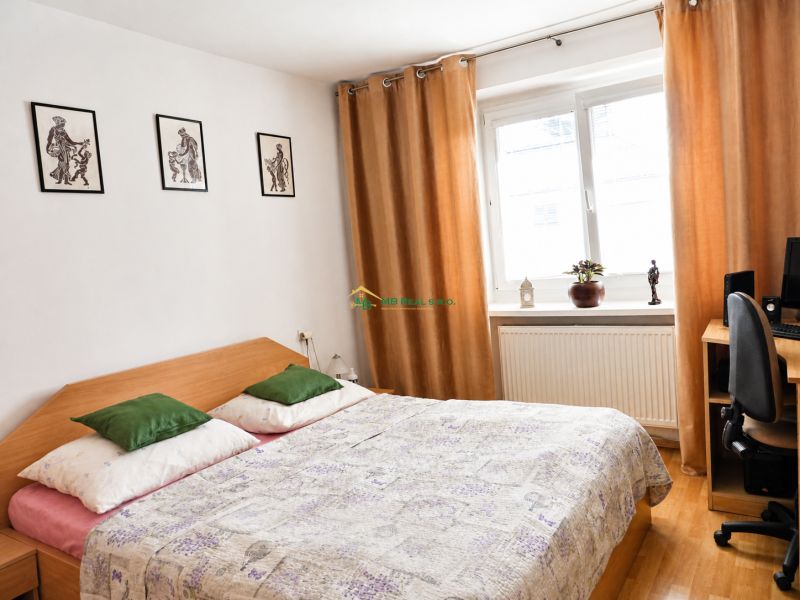 A bedroom in a 2-room apartment with a bed, a desk, and a wooden-patterned floor.