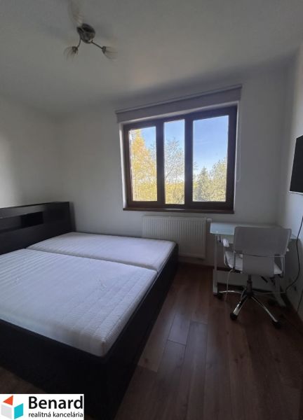 A bedroom with a bed, table, and wooden decor flooring in a three-room apartment.