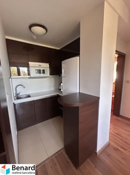 A kitchenette in a 3-room apartment with a wooden decor floor and dark cabinets.