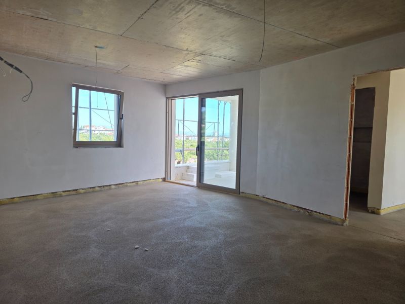 A room in a 3-bedroom apartment with a raw concrete floor and white walls.