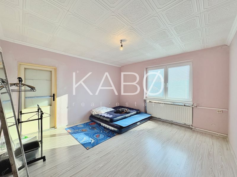 A room in a family house with a mattress on the floor, light pink walls, and a large window.