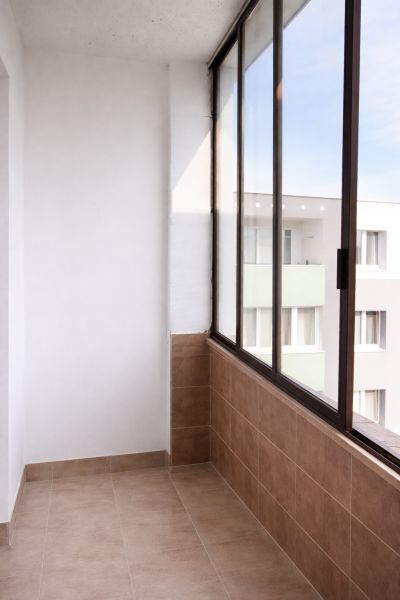 Glazed balcony in a 4-room apartment with light tiles and a view of the apartment building.