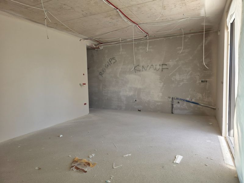 An unfinished room in a 3-room apartment with wires hanging from the ceiling.