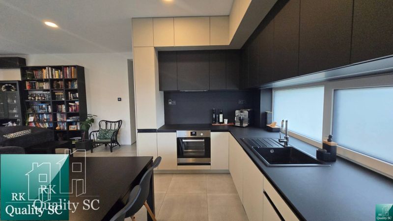 A kitchen with black cabinets and a bookshelf in a family house with a wood-patterned floor.