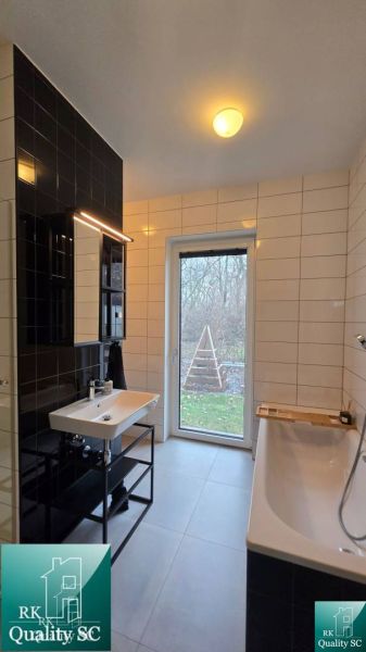 A bathroom with a bathtub and a sink in a family house, white and black tiles, a window with a view.