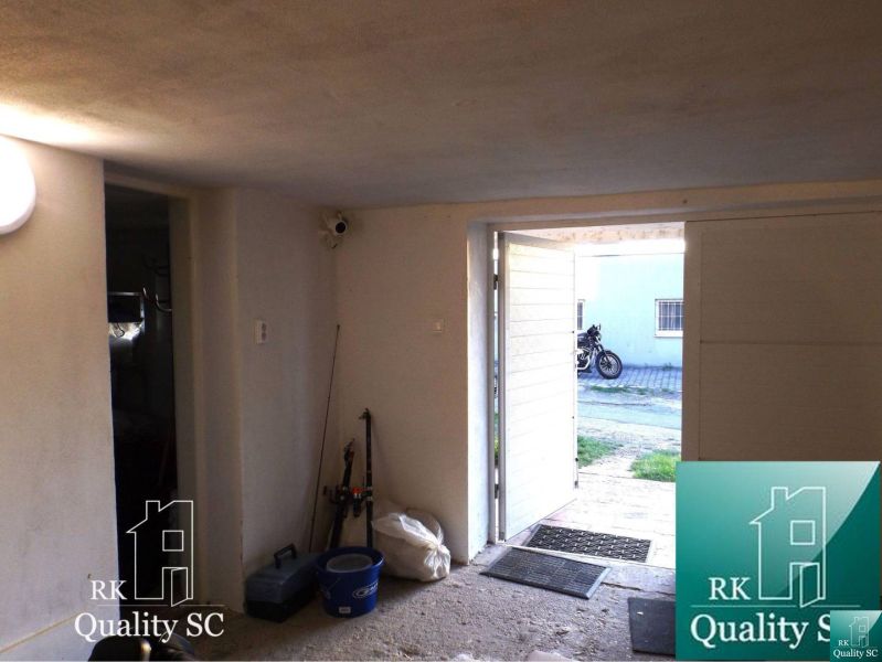 A garage room in a cottage with open doors shows a parked motorcycle outside.
