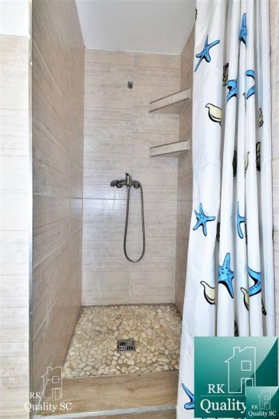 A shower corner with a pebble floor and a curtain with a sea motif in a cottage.