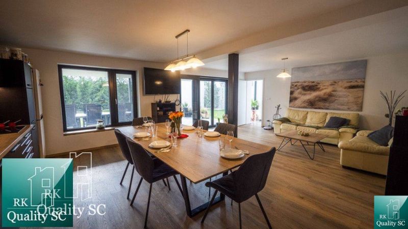 Living room with wood-patterned flooring in a family house, furnished with a dining table and a sofa.