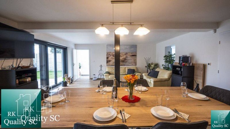 A dining table with glasses and plates in a family house, with a living room in the background.