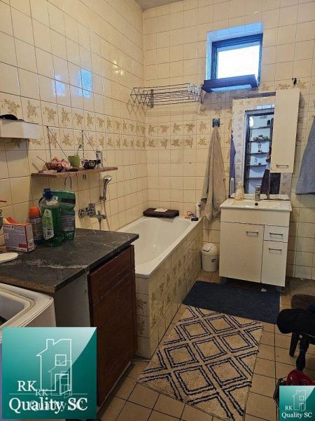 A bathroom in a family house with a bathtub, a sink, and storage cabinets. Tiled walls.