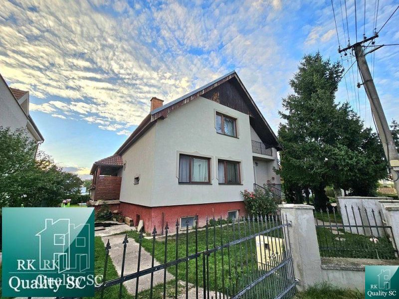 A family house on the street in Turna with a fenced plot and trees in the garden.