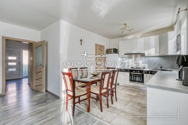 A kitchen in a family house with ceramic tiles, a wooden table, and white cabinets.