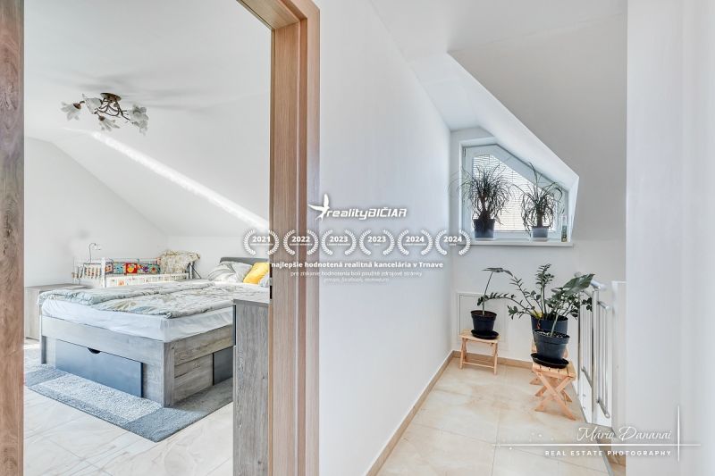 Attic bedroom with a bed and a window, plants on the staircase, family house.