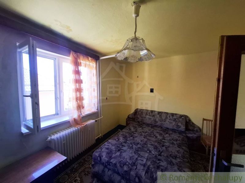 A room in a family house with a sofa, a window, and curtains in warm colors.