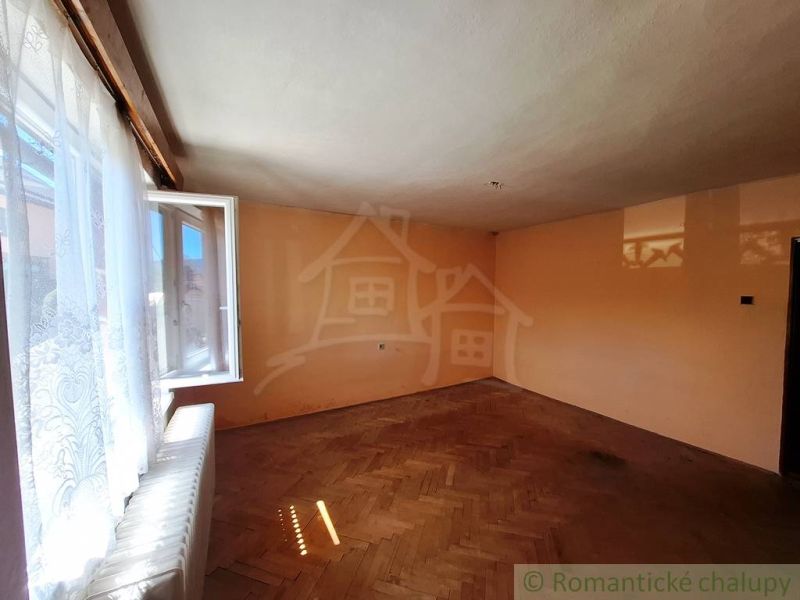 An open room with a wooden decor floor, a window with white curtains.