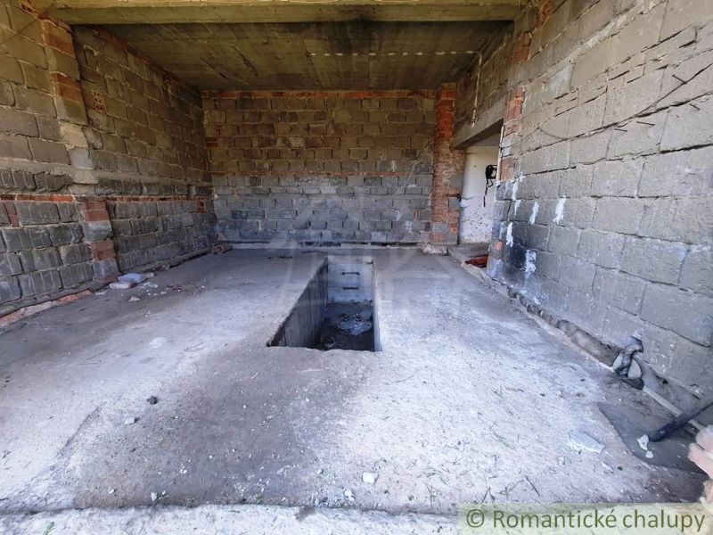 An unfinished garage in a family house with a service pit. Walls made of unplastered brick.