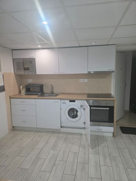 A kitchen in a one-room apartment with white kitchen cabinets and a wooden decor floor.
