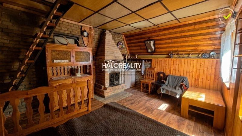 The interior of a cabin with a brick fireplace, stairs, and wooden decor on the walls and floor.