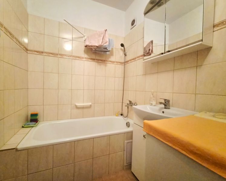 A bathroom with a shower and a sink in a 2-room apartment, tiled with light tiles.