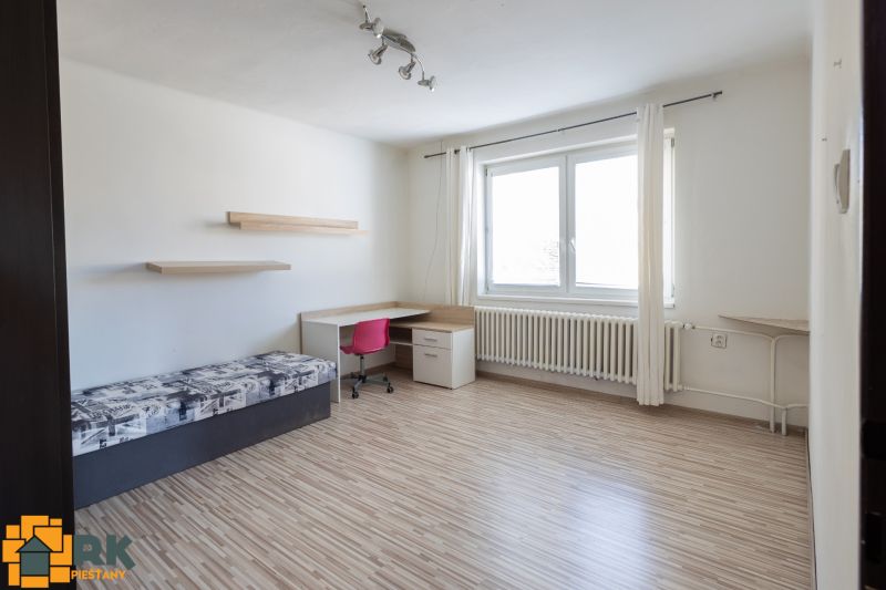 A room in a family house with a bed, a table, a pink chair, and a floor with a wooden decor.