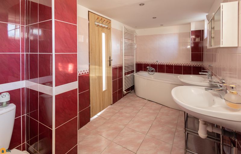 A bathroom with red tiles, a bathtub, and a double sink in a family house.